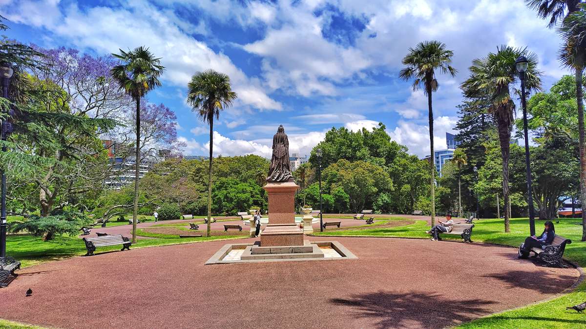 Die historische Queen-Victoria-Statue aus Bronze im Albert Park von Auckland umgeben von Palmen und Parkbänken.